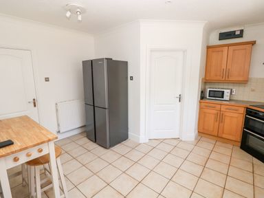 A kitchen with a wooden table and stools a refrigerator wooden cabinets microwave and oven at 1 Atlantic Haven in Llangennith