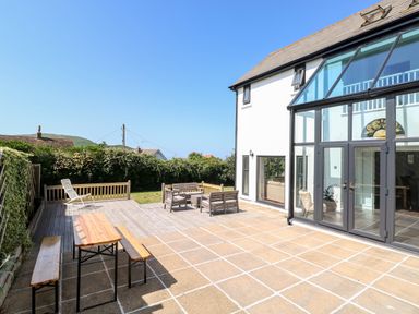 An outdoor patio with wooden benches and table next to a modern white building with large glass doors at 1 Atlantic Haven in Llangennith