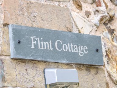 A gray stone sign with Flint Cottage on a stone wall above a light fixture at Flint Cottage in Swaffham