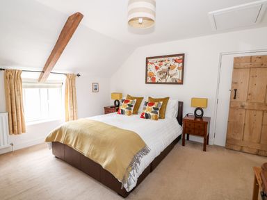 A bedroom with a double bed cushions bedside tables lamps a window with curtains and a wooden door at Flint Cottage in Swaffham