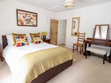 A bedroom with a bed with pillows and blankets a wooden door a chair a mirror and a dressing table at Flint Cottage in Swaffham