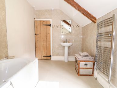A bathroom with a bathtub sink a wooden door a chest with towels and a heated towel rail at Flint Cottage in Swaffham