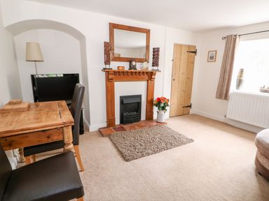 A living room with a wooden fireplace a small rug a wooden table two chairs a television lamp and a window at Flint Cottage in Swaffham