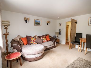 A lounge area with a round sofa and cushions a small table two chairs and wooden door at Flint Cottage in Swaffham