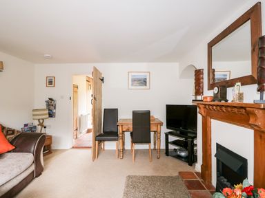 A living room with a sofa a wooden table with two chairs a television on a stand and a wooden fireplace at Flint Cottage in Swaffham