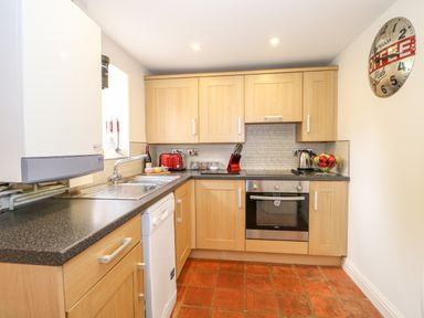 A kitchen with wooden cabinets a stainless steel oven a white dishwasher and a wall clock at Flint Cottage in Swaffham