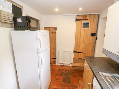 A kitchen area with a refrigerator topped by a microwave oven wooden doors a radiator and a countertop with a sink at Flint Cottage in Swaffham