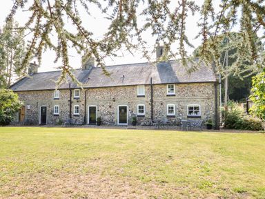 A stone cottage with several doors and windows a lawn and outdoor tables and chairs at Flint Cottage in Swaffham