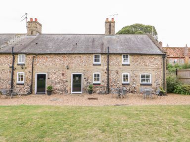 A stone cottage with black doors and windows a grassy lawn and outdoor seating at Flint Cottage in Swaffham