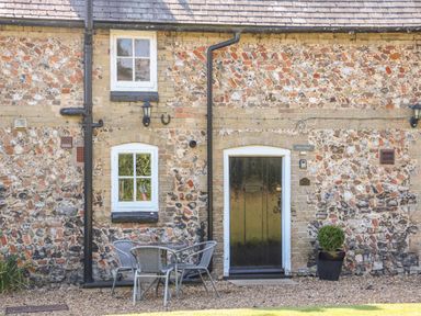 A stone cottage exterior with two windows a black door a small table with four chairs and a potted plant at Flint Cottage in Swaffham