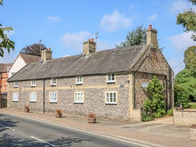 A street view of a long stone cottage with chimneys and white-framed windows at Flint Cottage in Swaffham