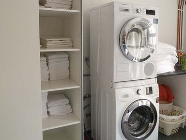 A laundry room with stacked washer and dryer and shelves with folded towels at Capel Dinorwig in Llanberis