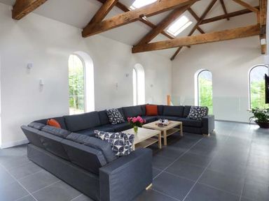A living room with a large dark grey sectional sofa wooden coffee tables and exposed wooden beams at Capel Dinorwig in Llanberis