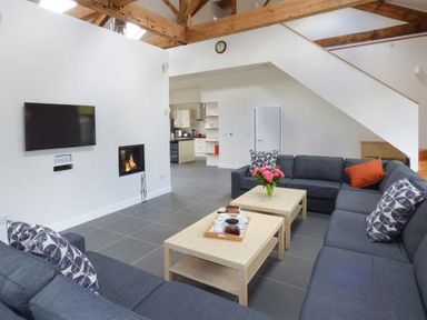 A living room with a sectional sofa two coffee tables a wall-mounted television and a fireplace at Capel Dinorwig in Llanberis