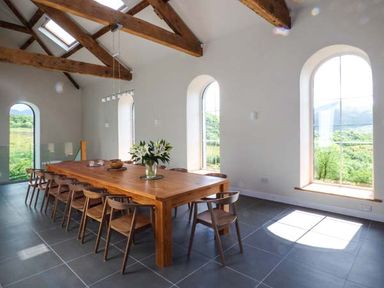 A dining room with a wooden table and chairs and large arched windows at Capel Dinorwig in Llanberis