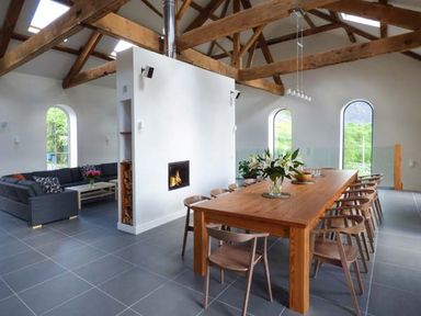 An open living and dining area with a wooden dining table and chairs a fireplace and a sectional sofa at Capel Dinorwig in Llanberis