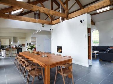 A dining area with a long wooden table and chairs next to a kitchen and a living room at Capel Dinorwig in Llanberis