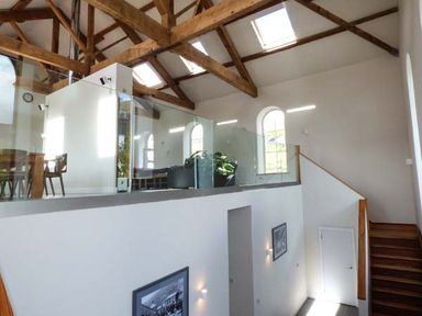 An interior view with wooden stairs leading to a mezzanine with glass railing wooden beams and skylights at Capel Dinorwig in Llanberis