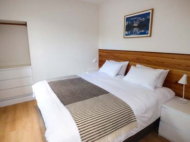 A bedroom with a double bed a wooden headboard two bedside tables with lamps a chest of drawers and a framed picture on the wall at Capel Dinorwig in Llanberis