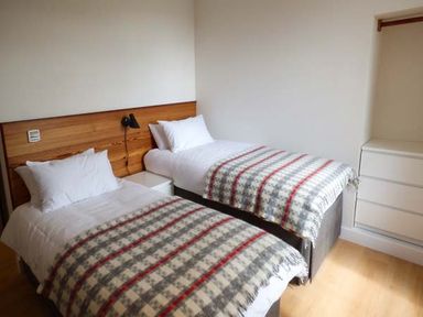A bedroom with two single beds a wooden headboard a bedside table and a chest of drawers at Capel Dinorwig in Llanberis