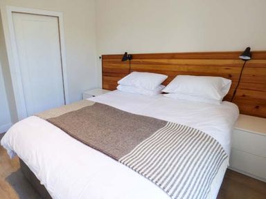 A bedroom with a bed with white bedding and a brown striped blanket and a wooden headboard with wall lamps at Capel Dinorwig in Llanberis