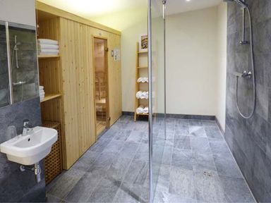 A bathroom with a wooden sauna, a shower area with glass partition, a sink, and shelves with towels at Capel Dinorwig in Llanberis