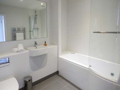 A bathroom with a bathtub shower combination a sink with towels and soap a wall mirror and a toilet at Capel Dinorwig in Llanberis