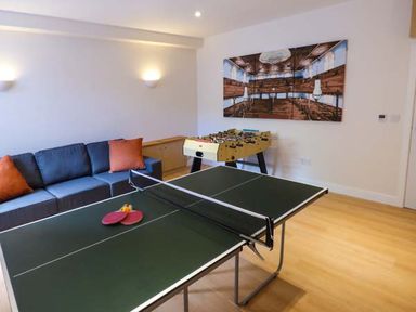 A game room with a ping pong table two paddles a couch with orange pillows and a foosball table at Capel Dinorwig in Llanberis