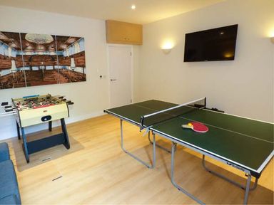 A room with a ping pong table with paddles and ball a foosball table a wall-mounted TV and a triptych wall art at Capel Dinorwig in Llanberis