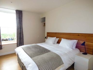 A bedroom with a double bed white bedding wooden headboard bedside table with lamp and window with curtains at Capel Dinorwig in Llanberis