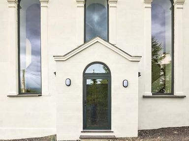 An exterior view of a building with a central arched door and tall narrow windows on each side at Capel Dinorwig in Llanberis