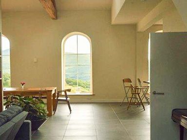 A dining area with a wooden table and chairs near arched windows with a view of hills at Capel Dinorwig in Llanberis
