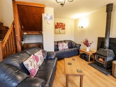 A living room with two leather sofas a wooden coffee table a wood burning stove and a wooden staircase at Bwthyn Fedwr Gog in Maerdy near Bala