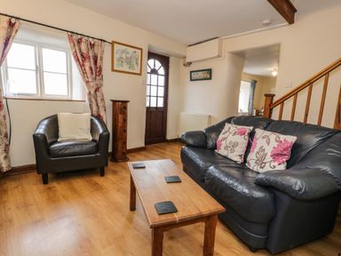 A living room with a black leather sofa and armchair a wooden coffee table and floral curtains at Bwthyn Fed'wr Gog in Maerdy near Bala