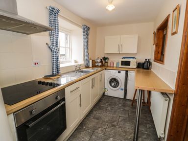 A kitchen with an oven sink washing machine microwave and a long countertop at Bwthyn Fed'wr Gog in Maerdy near Bala