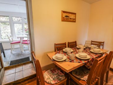 A dining area with a wooden table set with plates mugs and bowls and wooden chairs with floral cushions at Bwthyn Fedwr Gog in Maerdy near Bala