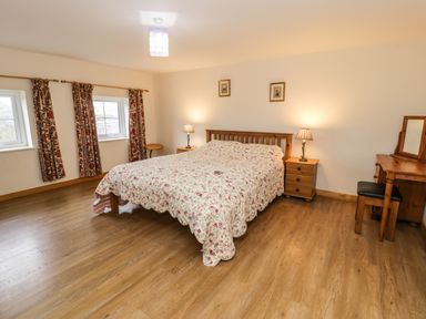 A bedroom with a double bed covered with a floral bedspread two bedside tables with lamps and a wooden dressing table with a stool at Bwthyn Fed'wr Gog in Maerdy near Bala