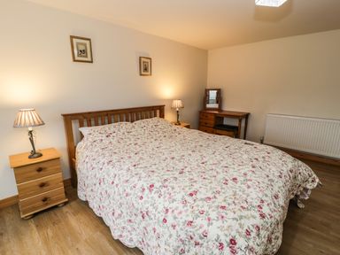 A bedroom with a wooden double bed with floral bedspread two bedside tables with lamps a wooden dressing table with a mirror and a radiator on the wall at Bwthyn Fed'wr Gog in Maerdy near Bala