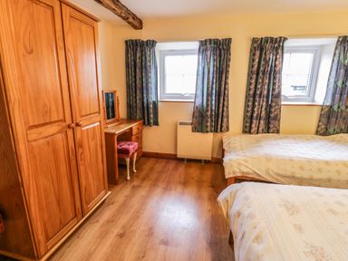 A bedroom with two single beds wooden wardrobe wooden dressing table and patterned curtains at Bwthyn Fed'wr Gog Maerdy near Bala