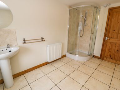 A bathroom with a shower enclosure pedestal sink radiator and wooden door at Bwthyn Fed'wr Gog in Maerdy near Bala