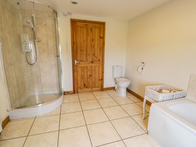 A bathroom with a shower, toilet, bathtub, wicker basket, and wooden door at Bwthyn Fed'wr Gog in Maerdy near Bala
