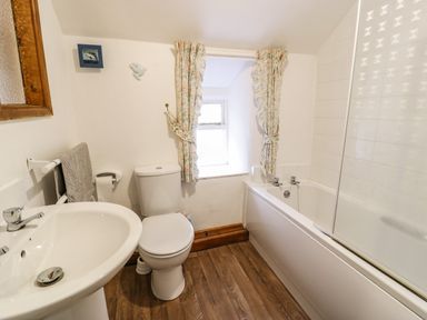 A bathroom with a sink toilet bathtub window and floral curtains at Bwthyn Fedwr Gog Maerdy near Bala