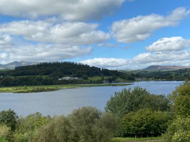 A landscape with a lake surrounded by trees and hills under a partly cloudy sky at Bwthyn Fed'wr Gog in Maerdy near Bala