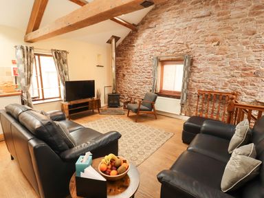 A living room with a sofa, television and wooden beams at Stable Cottage in Bolton Low Houses