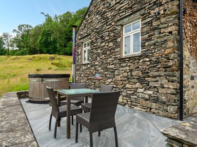 An outdoor seating area with a hot tub and a table with chairs at Dove Cottage at the Graythwaite Estate near Hawkshead