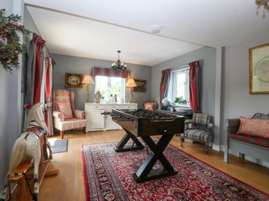 A room with a foosball table on a red patterned rug and various chairs at Nant-yr-Rhedyn in Red Wharf Bay