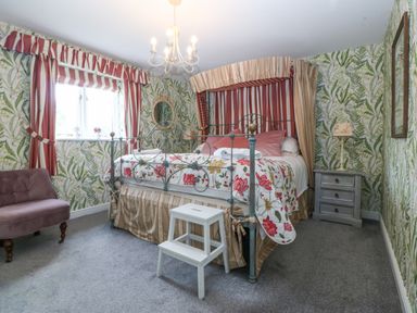 A bedroom with a metal bed frame floral bedding striped curtains and a gray nightstand at Nant-yr-Rhedyn in Red Wharf Bay