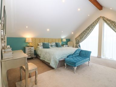 A bedroom with a large bed blue bench bedside tables lamps and a dressing table at Nant-yr-Rhedyn in Red Wharf Bay