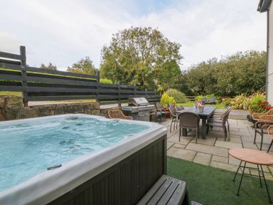 An outdoor patio area with a hot tub table and chairs a barbecue grill and garden furniture at Nant-yr-Rhedyn in Red Wharf Bay