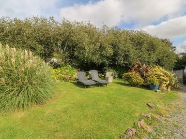 A garden with lawn chairs and plants near a gravel driveway at Nant-yr-Rhedyn in Red Wharf Bay